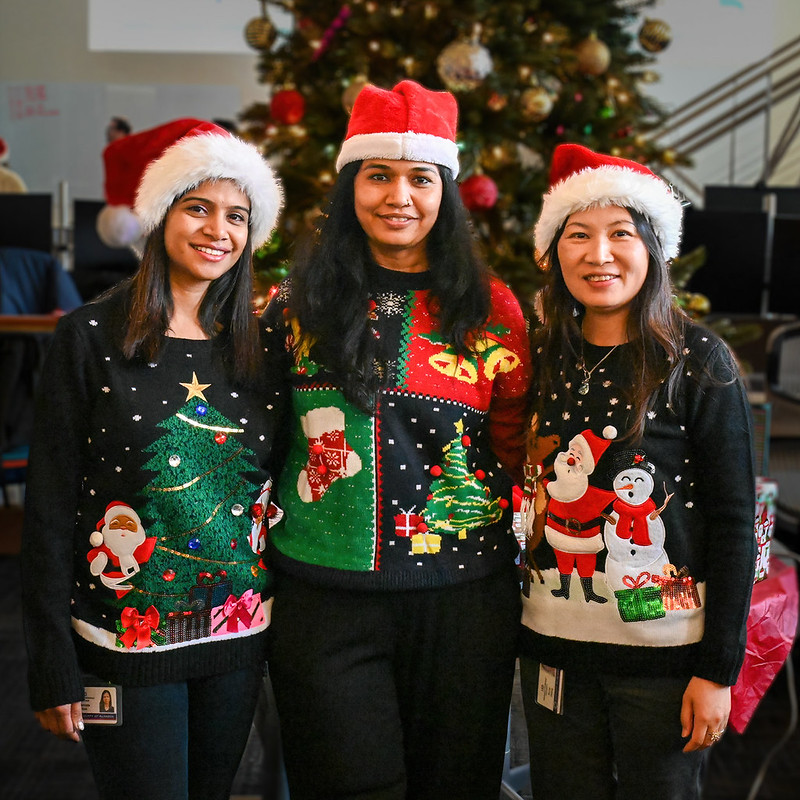2025 Holiday Party; 3 women in Santa hats in front of a Christmas tree
